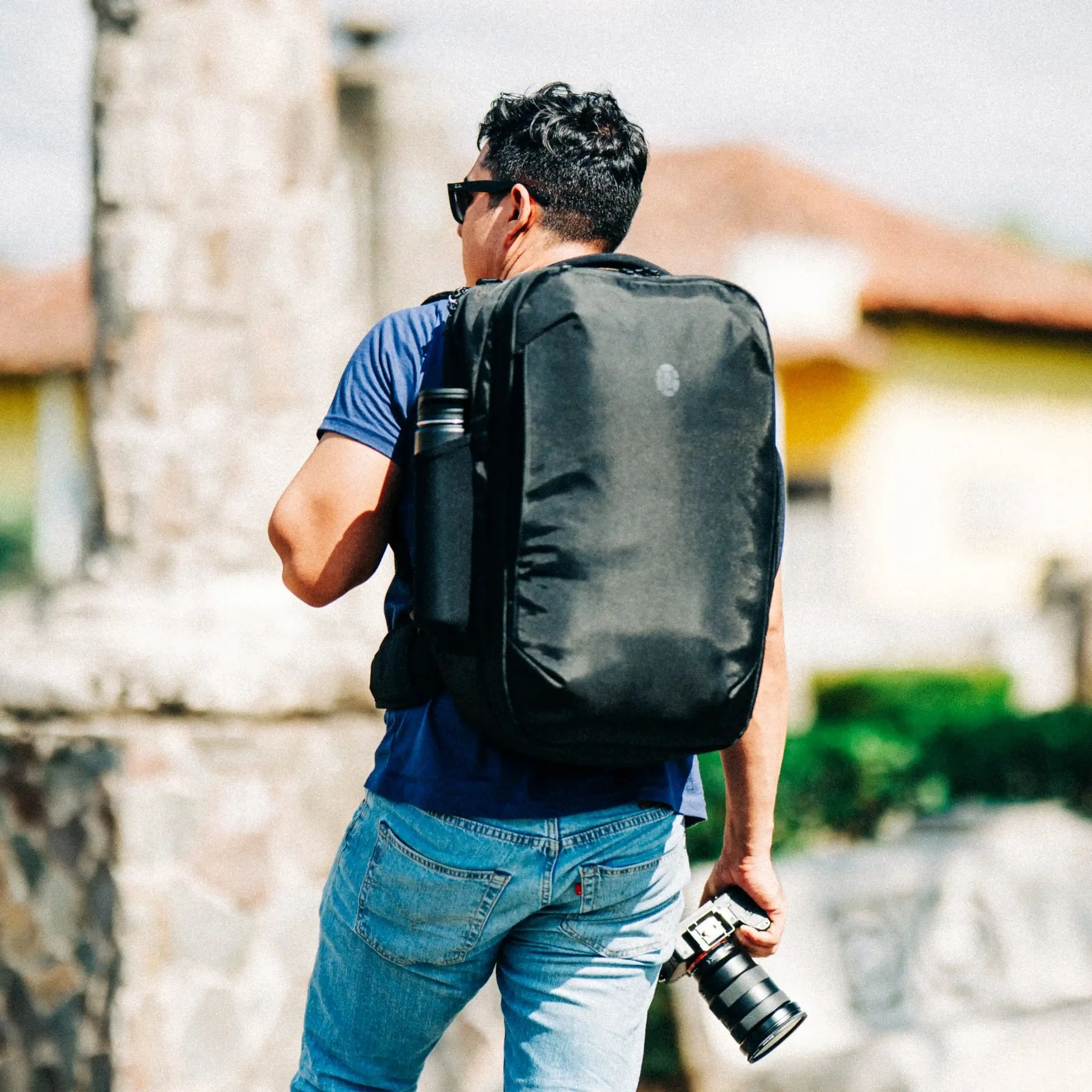 A traveler walks through an old town with a Tortuga backpack and a camera
