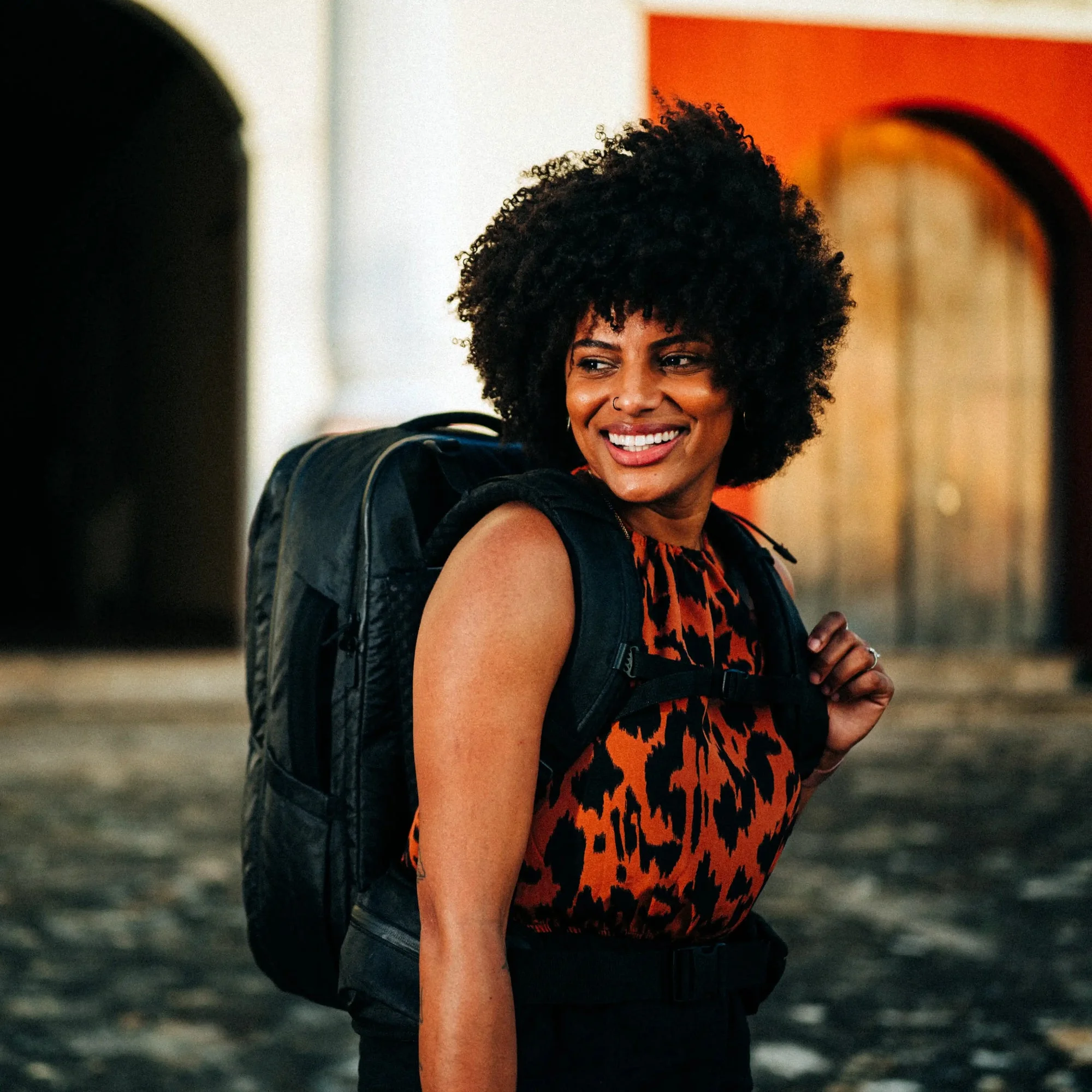 A smiling traveler wearing a Tortuga backpack on a city street