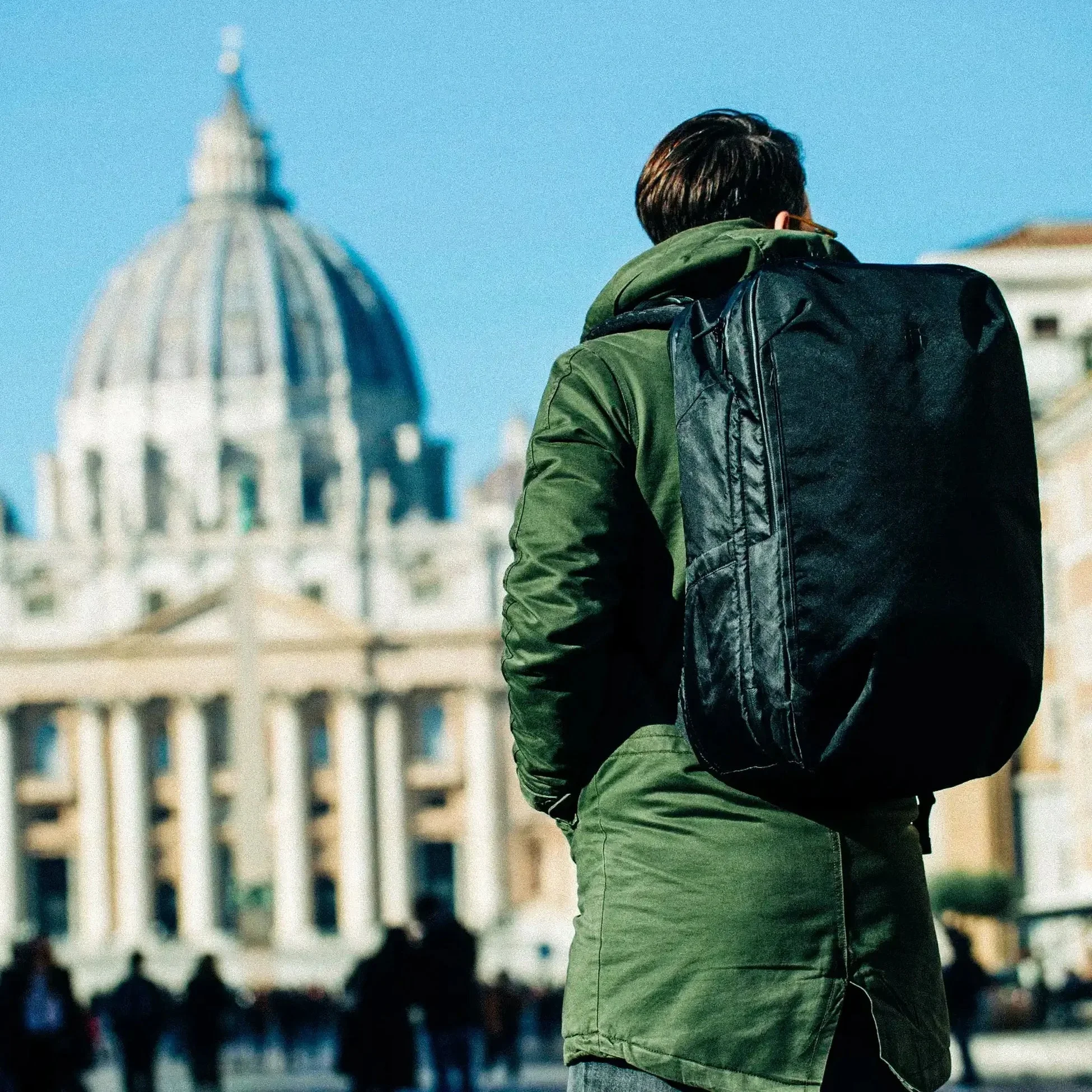 A traveler in a green jacket wearing a Tortuga backpack in front of a domed cathedral